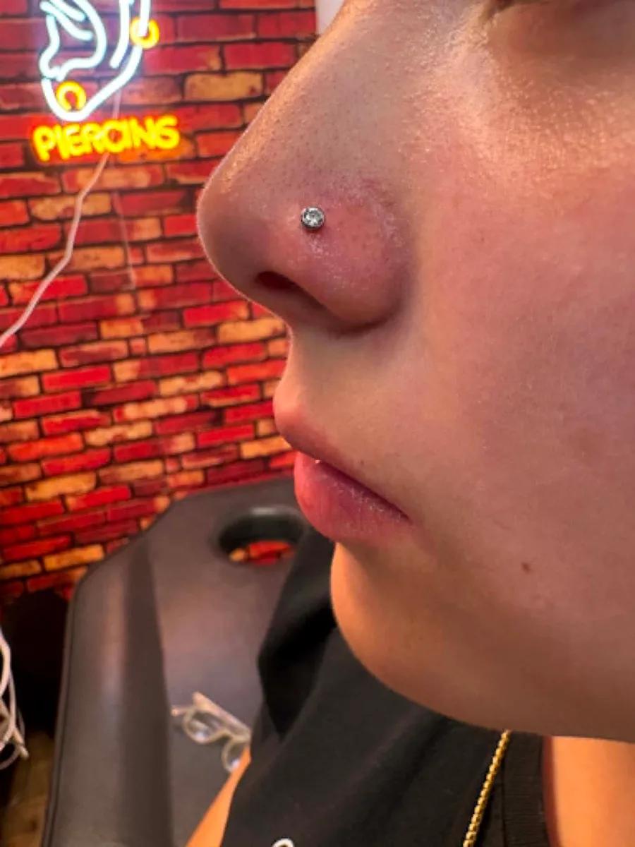 Fresh nostril piercing with a crystal stud in front of the shop piercing sign
